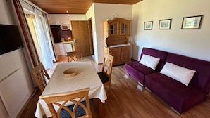A compact living space with a dining area, a purple sofa, and a wooden cabinet. - Cosy Apartment in Gortipohl With Garden (Sankt Gallenkirch)