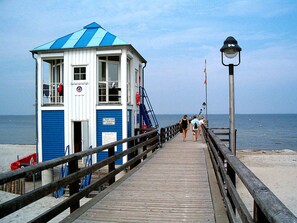 A wooden pier leading to a lifeguard tower with a blue and white color scheme, a railing, and a view of the sea. - to the Beach Comfortable Holiday Residence (Lubmin)