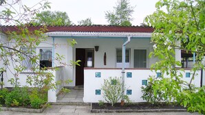 A small, single-story building with a white exterior and a red roof. It features a front porch with a small step leading to the entrance, and a window on the right side. - to the Beach Comfortable Holiday Residence (Lubmin)