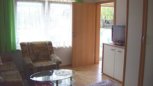 A living room with a sofa, a glass coffee table, a television on a cabinet, and a door leading to an outdoor area. - to the Beach Comfortable Holiday Residence (Lubmin)