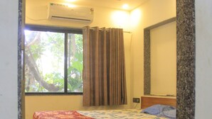 A bedroom with a bed, an air conditioner, a ceiling fan, a window with curtains, and a view of greenery outside. - ROSHNI - THE LUXURY GUEST HOUSE (Baga)