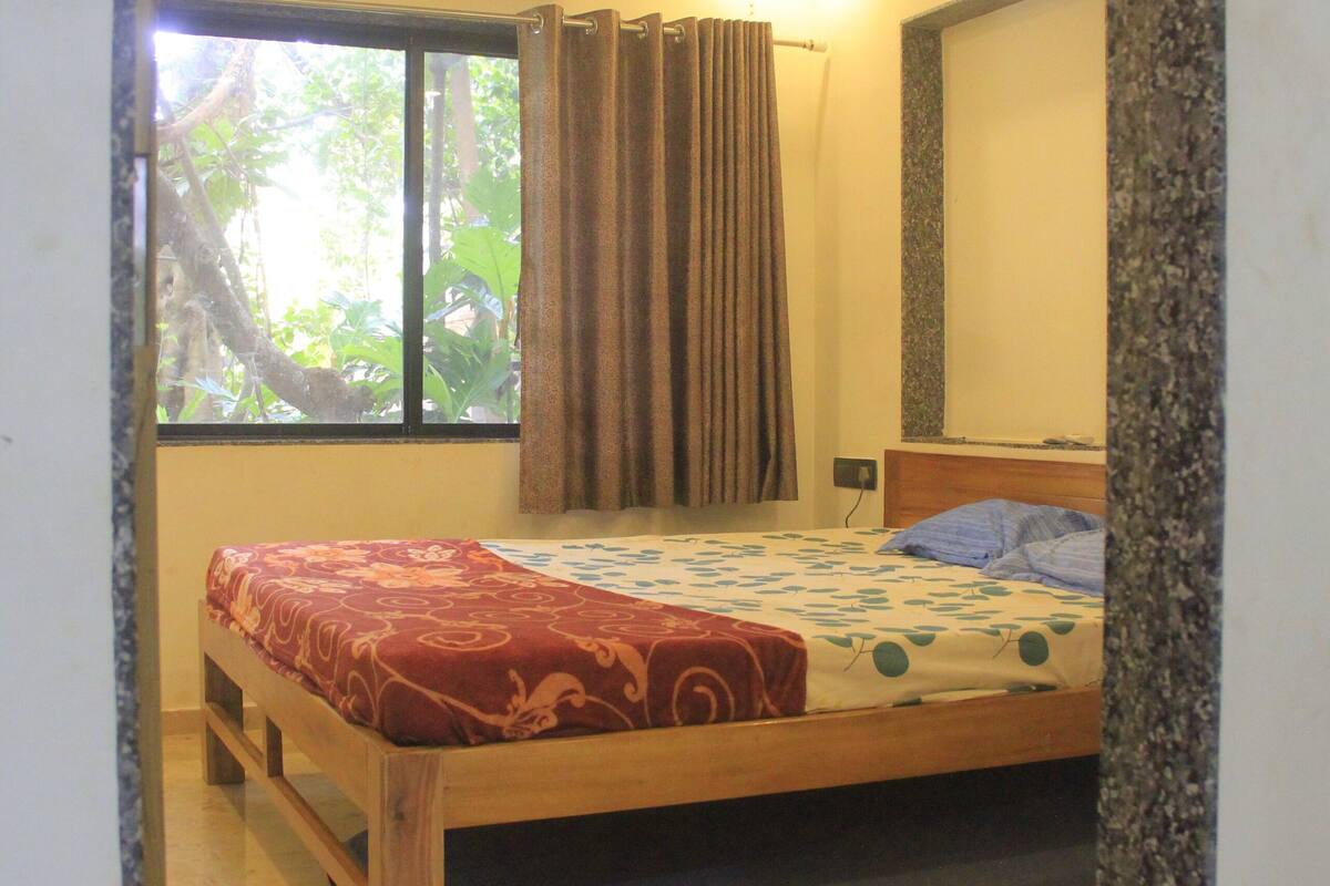 Un dormitorio con cama, aire acondicionado, ventilador de techo, ventana con cortinas y vistas a zonas verdes.