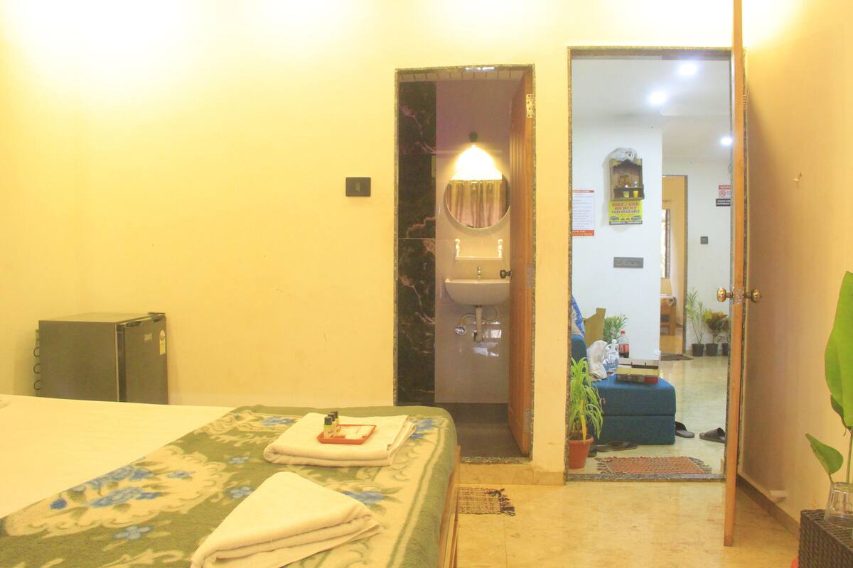 Habitación de hotel con cama, mesita de noche, espejo y baño visible a través de una puerta abierta.