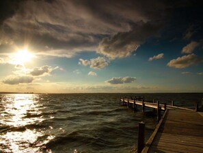 A wooden pier extending into a body of water with the sun shining through the clouds. - Luerssen Lindenhopsweg (Wunstorf)