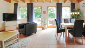 A modern living room with a sofa, a TV, a dining table with chairs, and large windows with curtains. - Luerssen Lindenhopsweg (Wunstorf)