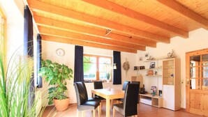 A dining area with a wooden ceiling, a table with chairs, a potted plant, and a cabinet with glass doors. - Luerssen Lindenhopsweg (Wunstorf)