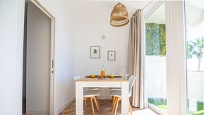 A dining area with a white table and chairs, a wicker pendant light, and a view of greenery outside. - Sunstay Portview Marina Flat II Benalmadena (Benalmádena)