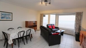 A living room with a dining area, a sofa, a coffee table, and a view of the sea. - Beachfront Stay in Middelkerke for 6 (Middelkerke)