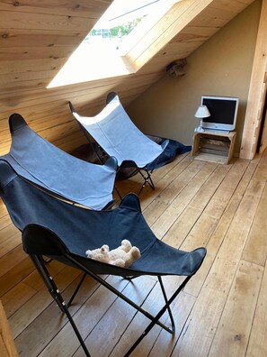 A cozy attic room with wooden flooring, two foldable chairs, a small table with a lamp, and a television. - Holiday Home in Sprimont With Forest (Sprimont)