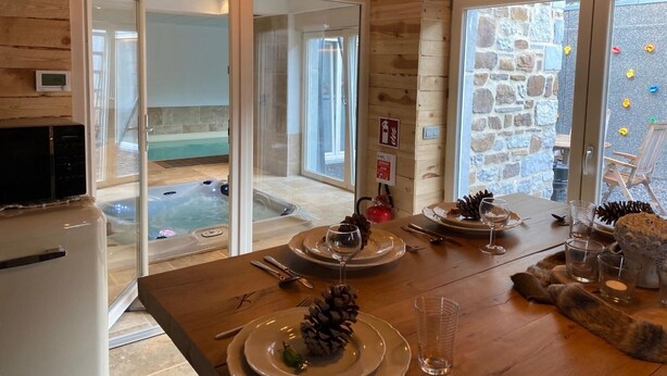 A wooden interior with a dining table set for two, a spa area visible through glass doors, and a stone wall with climbing plants. - Holiday Home in Sprimont With Forest (Sprimont)