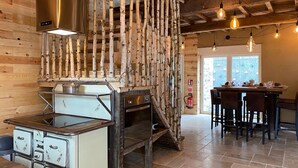 A rustic kitchen with wooden walls, a stove, and a dining area with a table and chairs. - Holiday Home in Sprimont With Forest (Sprimont)
