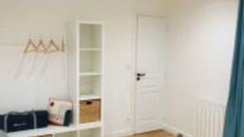 Una habitación con piso de madera, una puerta blanca, un estante blanco y una cortina azul.