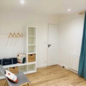 A room with a wooden floor, a white door, a white shelving unit, and a blue curtain. - Le Domaine des Figuiers - Le Gîte des Pèlerins (Servon)