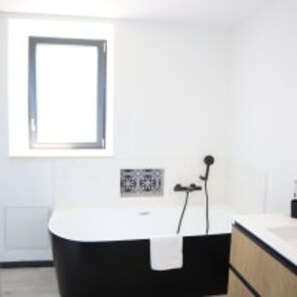A modern bathroom with a freestanding bathtub, a small window, and a wall-mounted sink. - Le Domaine des Figuiers - Le Gîte des Pèlerins (Servon)