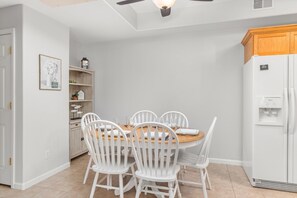 Une cuisine avec une table à manger, des chaises blanches, un réfrigérateur blanc et un meuble en bois.