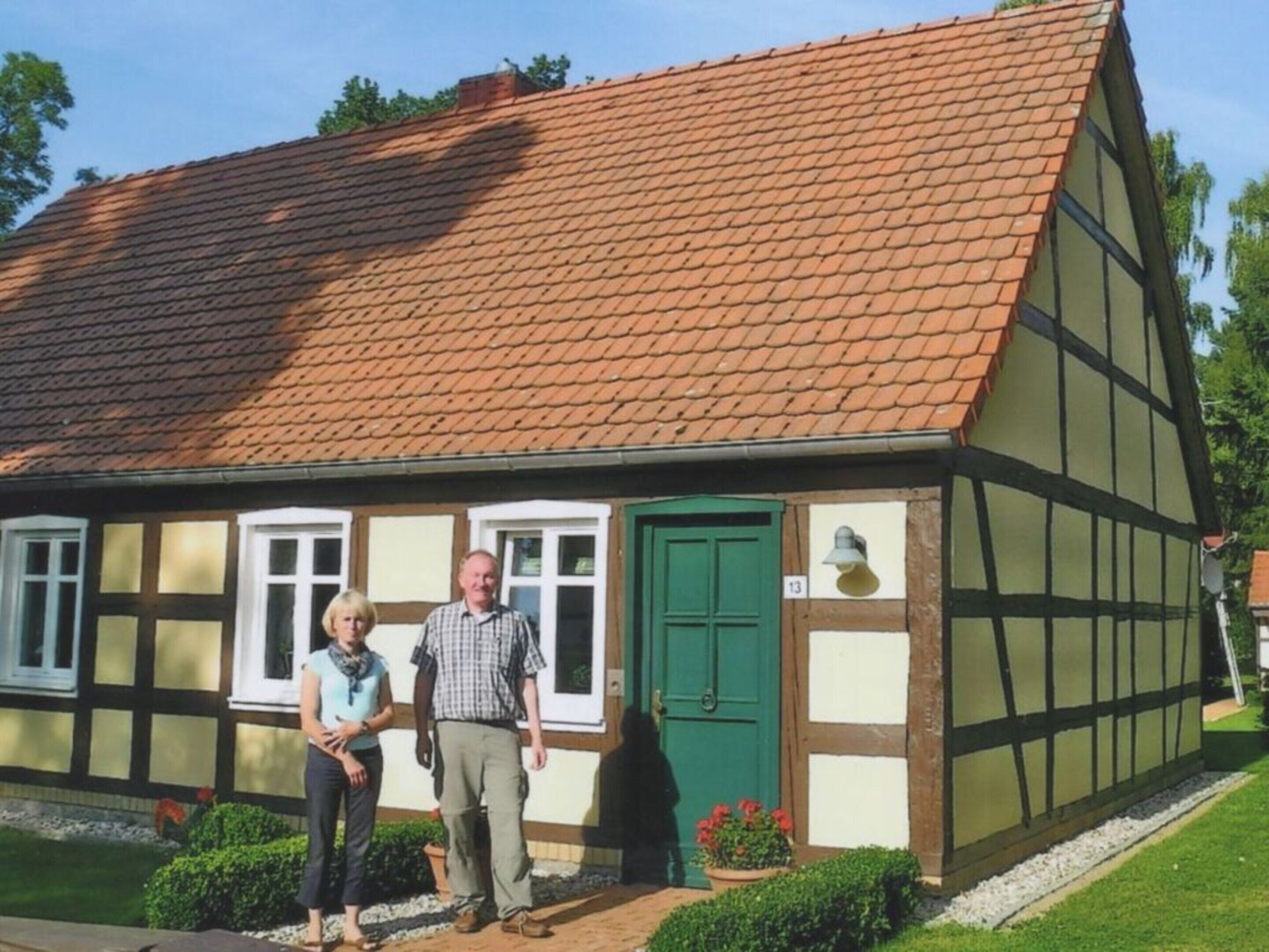 Ein traditionelles Fachwerkhäuschen mit Ziegeldach, einer grünen Tür und einem kleinen Garten mit Blumentöpfen.