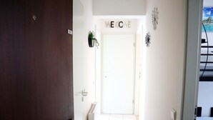 Un couloir avec une porte blanche sur laquelle est écrit « BIENVENUE », une petite plante et des œuvres d’art décoratives accrochées au mur.