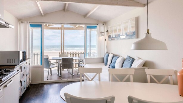 Une pièce située en bord de mer, comprenant un coin repas, une cuisine et de grandes fenêtres donnant sur la plage.