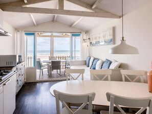 A coastal room with a dining area, kitchen, and large windows overlooking the beach.