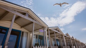 Une rangée de maisons de plage dotées d’une terrasse en bois, sous un ciel dégagé.