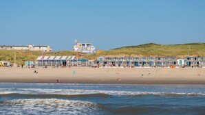 Un hôtel situé en bord de mer, composé de plusieurs bâtiments aux toits bleus, avec une plage de sable et une dune herbeuse en arrière-plan.