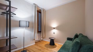 Una habitación con un sofá verde, una lámpara de pie, una lámpara de mesa, un perchero y suelo de madera.