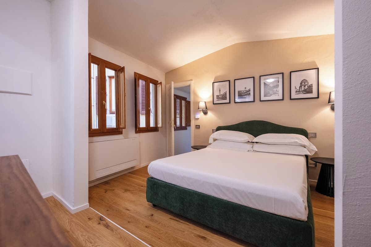 A bedroom with a large bed, wooden flooring, a green headboard, and framed pictures on the wall.