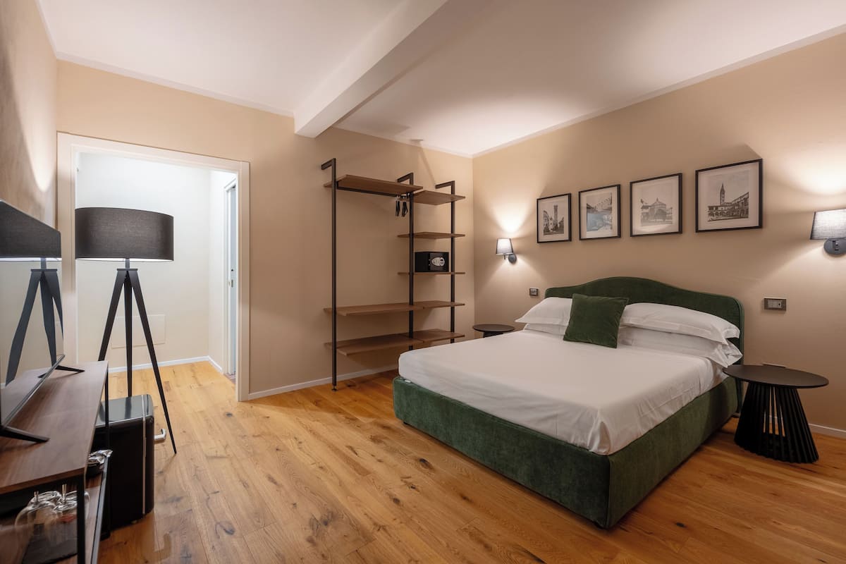 A bedroom with a bed, a desk, a lamp, a shelf unit, and wall-mounted lights.
