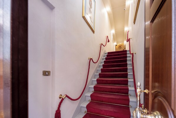 A staircase with red carpeting and gold railings, leading to a door with a brass handle. - Palazzina Fusi (Florence)