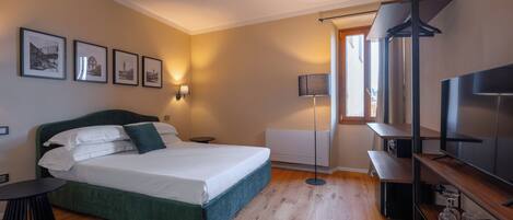 A bedroom with a bed, bedside tables, a floor lamp, a TV, and framed pictures on the wall.