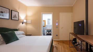 Habitación de hotel con cama, televisión, escritorio y baño visible a través de una puerta abierta.