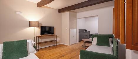 A compact room with two single beds, a small desk with a TV, a kitchenette, and a dining area.