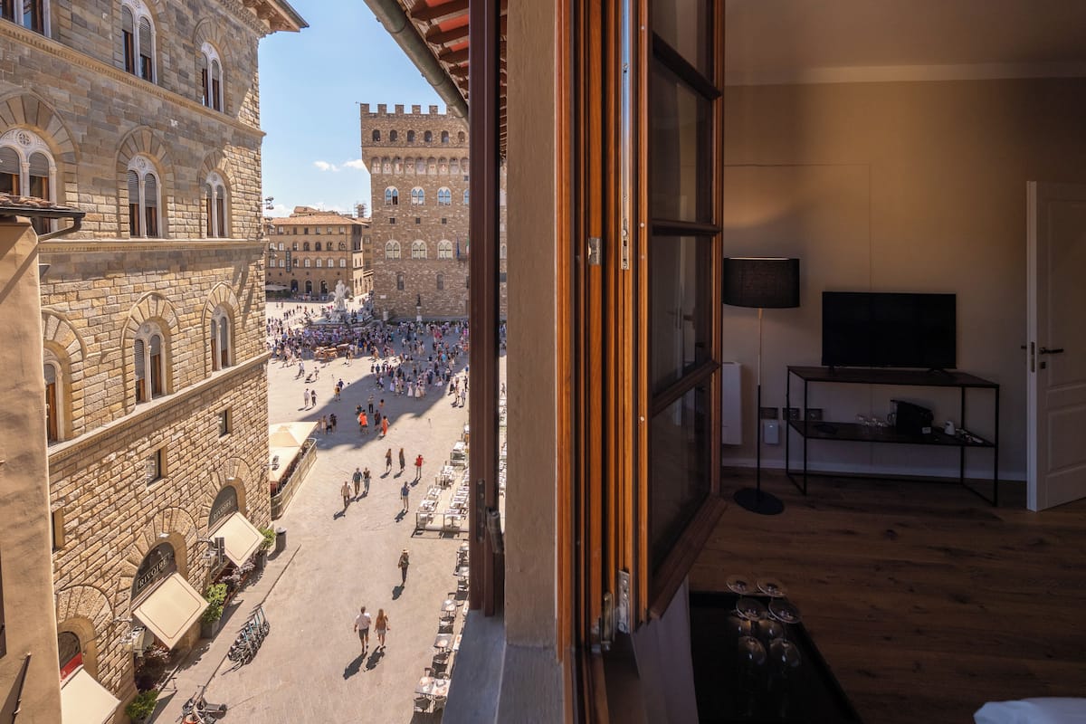 A room with a large window overlooking a crowded square with historic buildings.