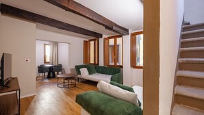 Un amplio salón con piso de madera, un sofá verde, un sofá blanco, una mesa de comedor con sillas y una escalera.