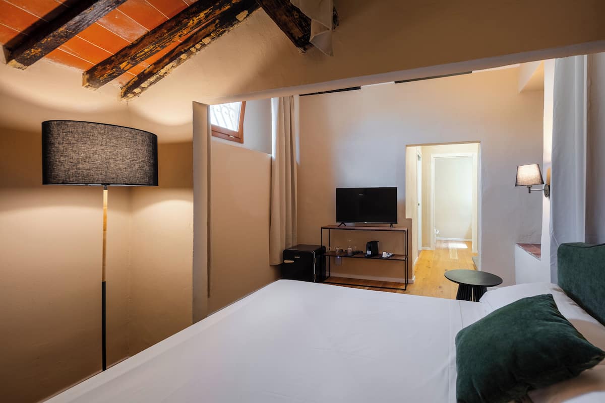 A hotel room with a bed, a TV, a lamp, and a small table.