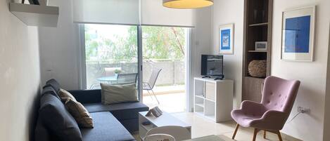 A modern living room with a sofa, a pink chair, a glass table, and a TV on a stand.