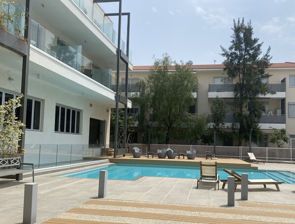 A modern building with a swimming pool, outdoor seating, and a view of neighboring buildings.