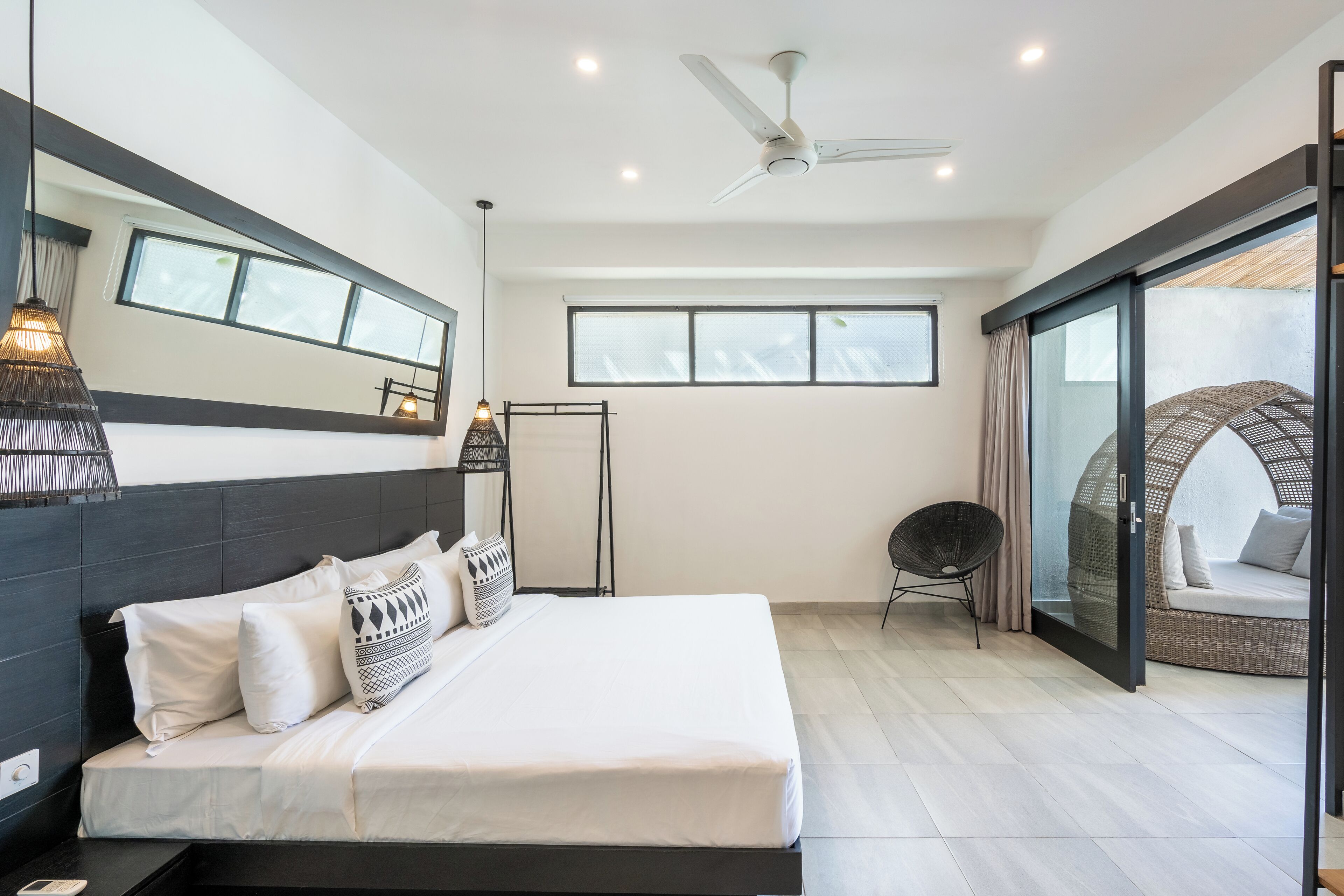 A modern bedroom with a large bed, a ceiling fan, and a view of a balcony with a wicker chair.