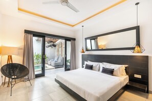Ein modernes Hotelzimmer mit einem großen Bett, einem Sessel, einem Balkon mit Vorhängen und einem Deckenventilator.