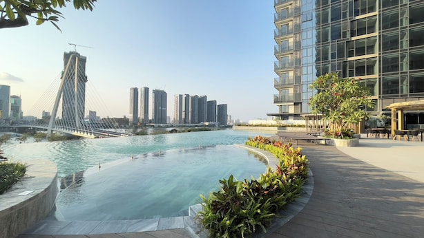 A modern building with a rooftop pool, surrounded by greenery and overlooking a river with a bridge in the background. - The Opera Residence Bitexco view (Ho Chi Minh City)