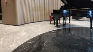 A grand piano in a spacious, modern lobby with a curved marble floor and vertical wooden paneling. - The Opera Residence Bitexco view (Ho Chi Minh City)