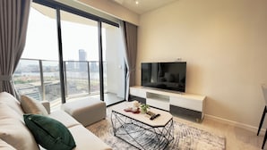 A modern living room with a large TV, a sofa, a coffee table, and a view of a cityscape through large windows. - The Opera Residence Bitexco view (Ho Chi Minh City)