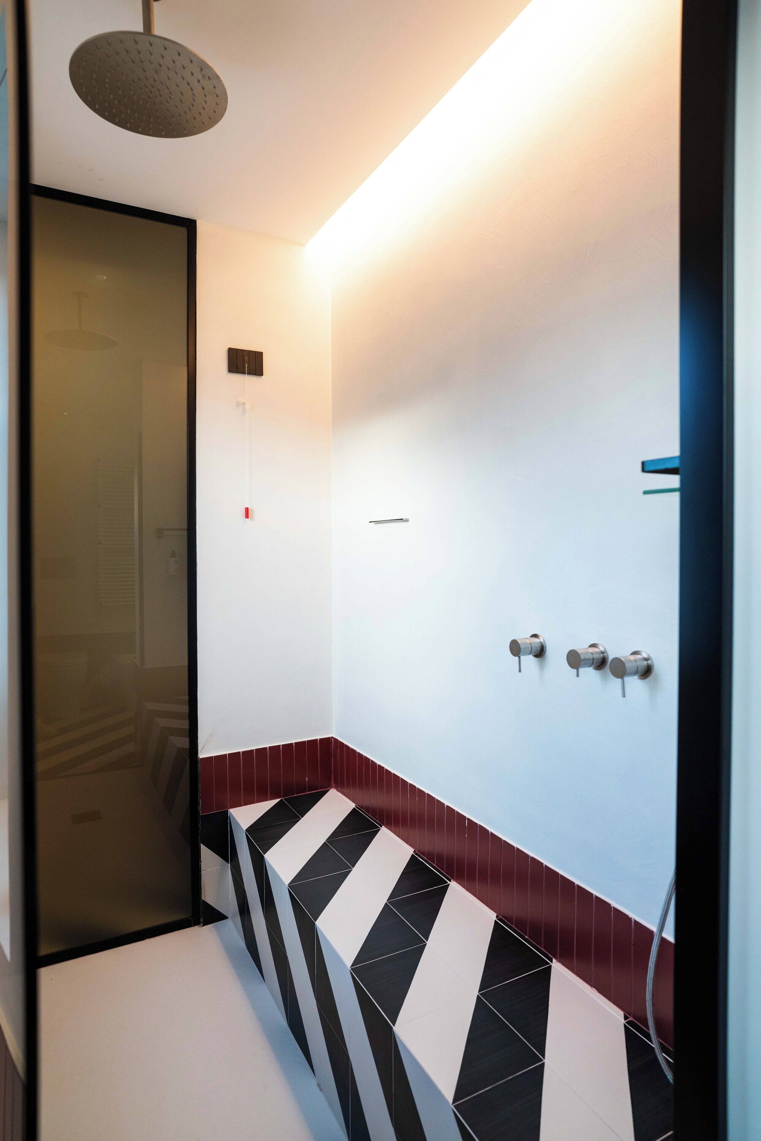 A modern bathroom with a glass door, a shower with a round head, and a tiled floor with a black and white pattern.