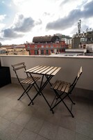 Een dakterras met een houten tafel en twee stoelen, met uitzicht op een stadsbeeld met gebouwen en een heuvel op de achtergrond.