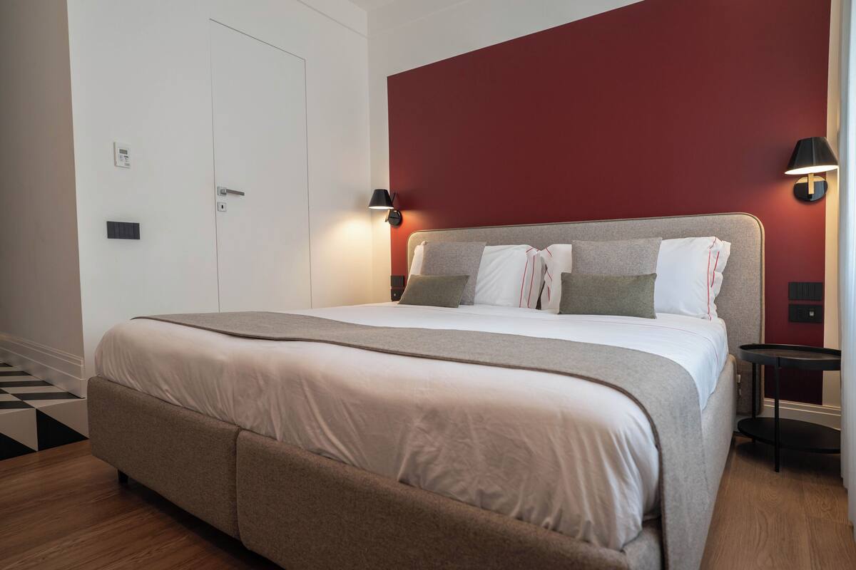 A neatly made bed with a headboard, a bedside table with a lamp, and a door with a lock.