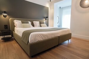 Une chambre d’hôtel moderne avec un grand lit, une table de chevet, une lampe fixée au mur et une fenêtre avec des rideaux.