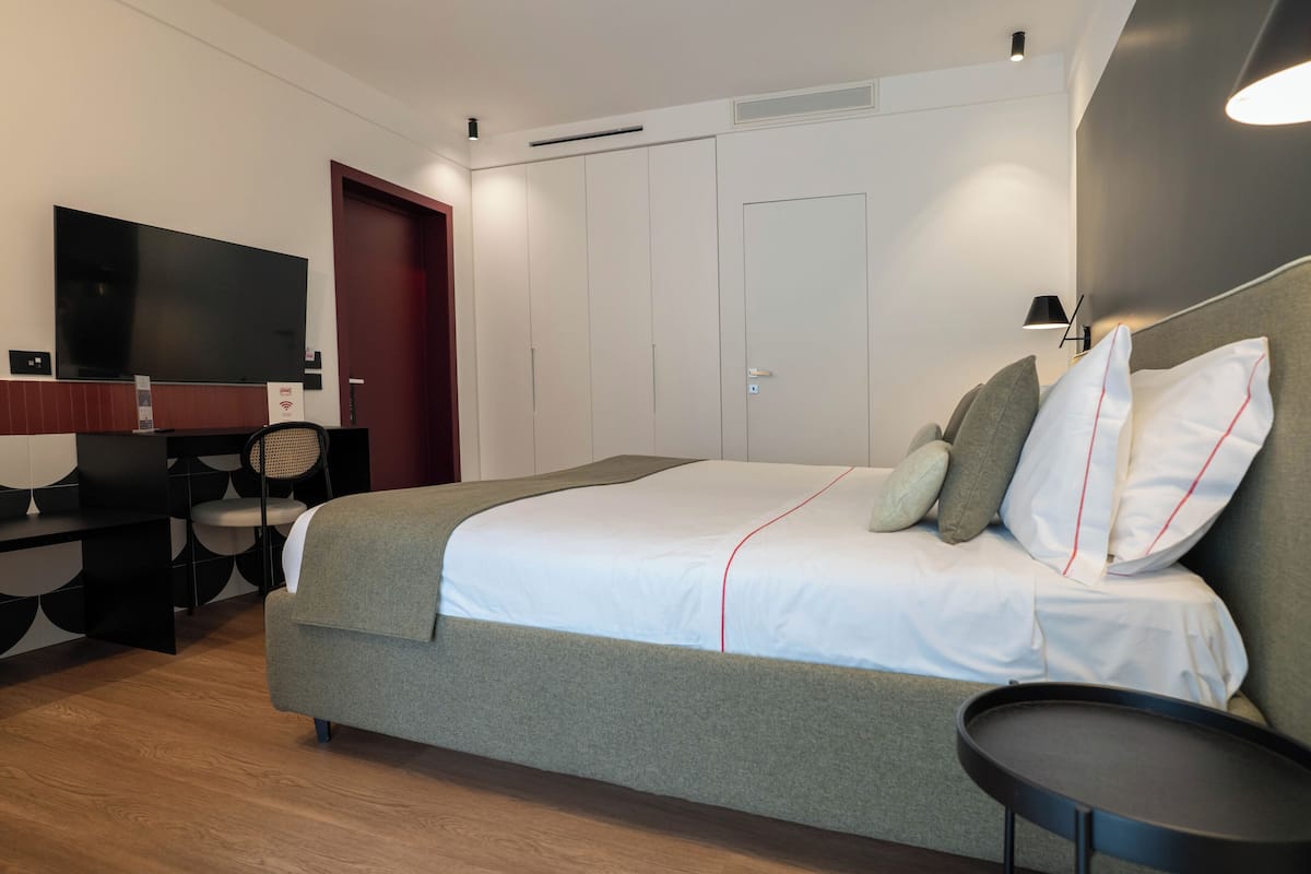 A modern hotel room with a bed, a desk, a flat-screen TV, and a wardrobe.