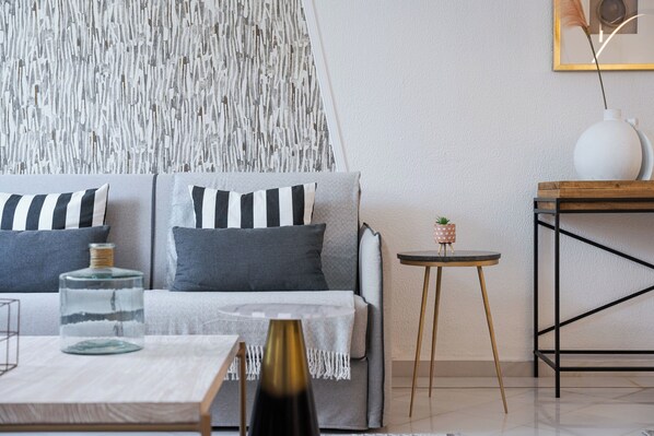 Un salon moderne avec un canapé gris, des coussins à rayures, un vase en verre et une petite table sur laquelle est posée une plante.