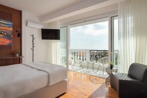 Une chambre avec un lit, une télévision, un balcon avec vue et un fauteuil.
