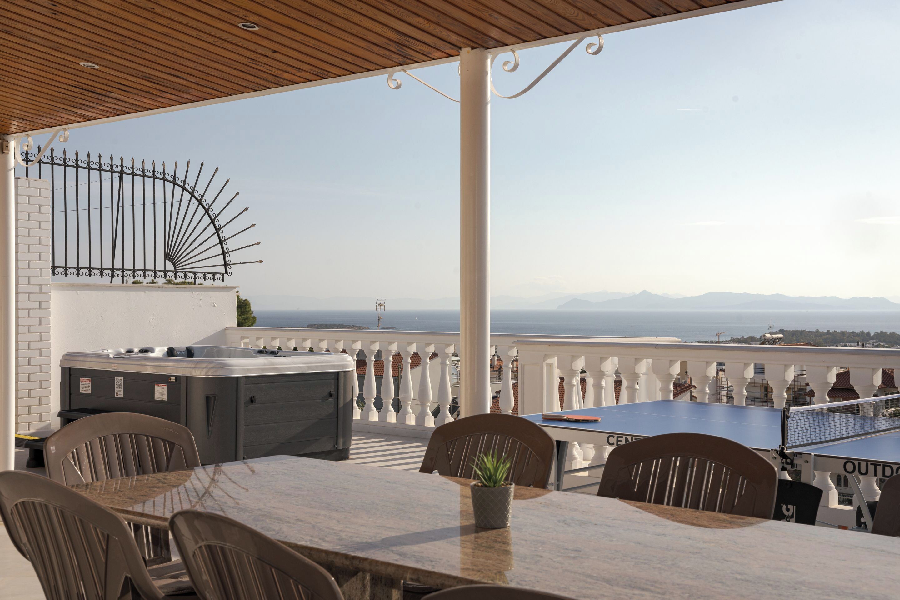 A rooftop terrace with a hot tub, outdoor seating, and a scenic view of the sea and mountains.